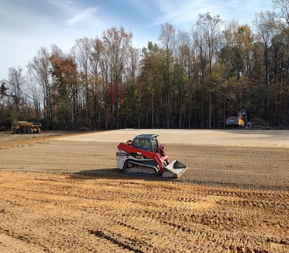 A skid steer compact loader levels dirt in an open field, with trees in the background.