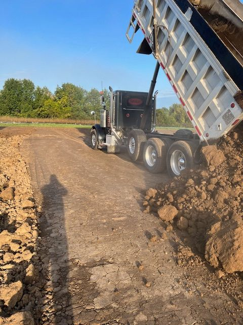 A dump truck unloading soil onto a dirt road under a blue sky, setting the stage for construction.