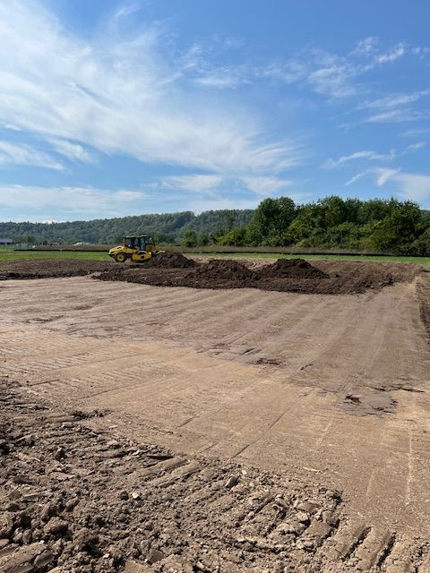 Construction site with a soil compactor working on a dirt field under a blue sky.