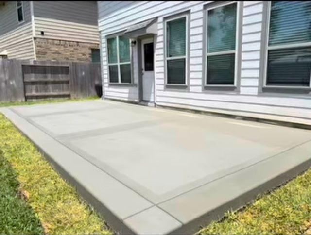 Concrete patio outside a house, with grass border and windows visible.