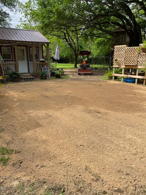 A small yard with a shed, play structure, and bare earth ground. Green trees and a fence are in the background.