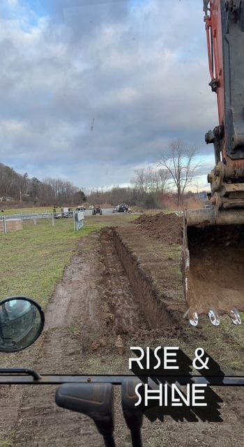Excavator digging a trench in a field on an overcast day. 