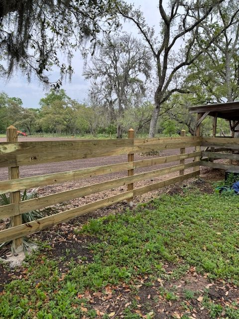 Wooden split-rail fence in a grassy area, with trees in the background.