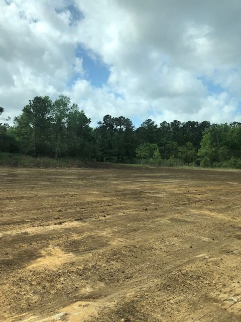 Cleared dirt field with treeline and cloudy sky.