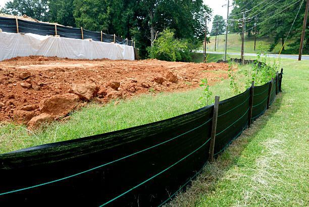 Construction site with erosion control; dirt, black silt fence, and green grass.