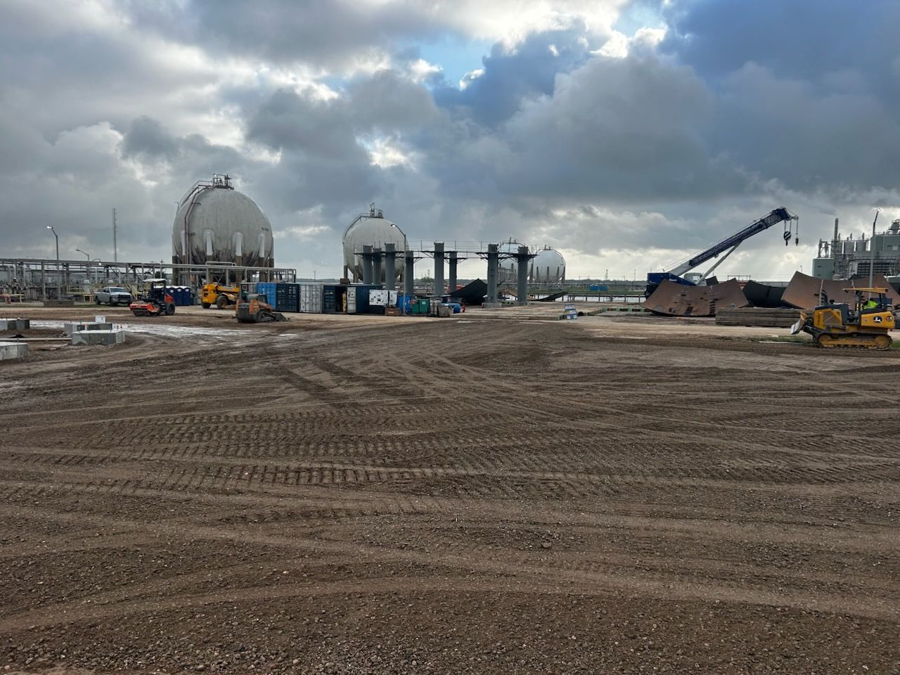 Construction site with tanks, heavy machinery, and cloudy sky.