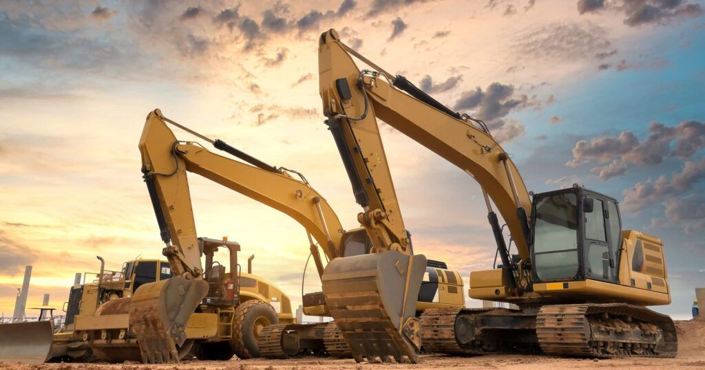 Overgrown field with green foliage, brown dirt, and trees under a blue and cloudy sky.