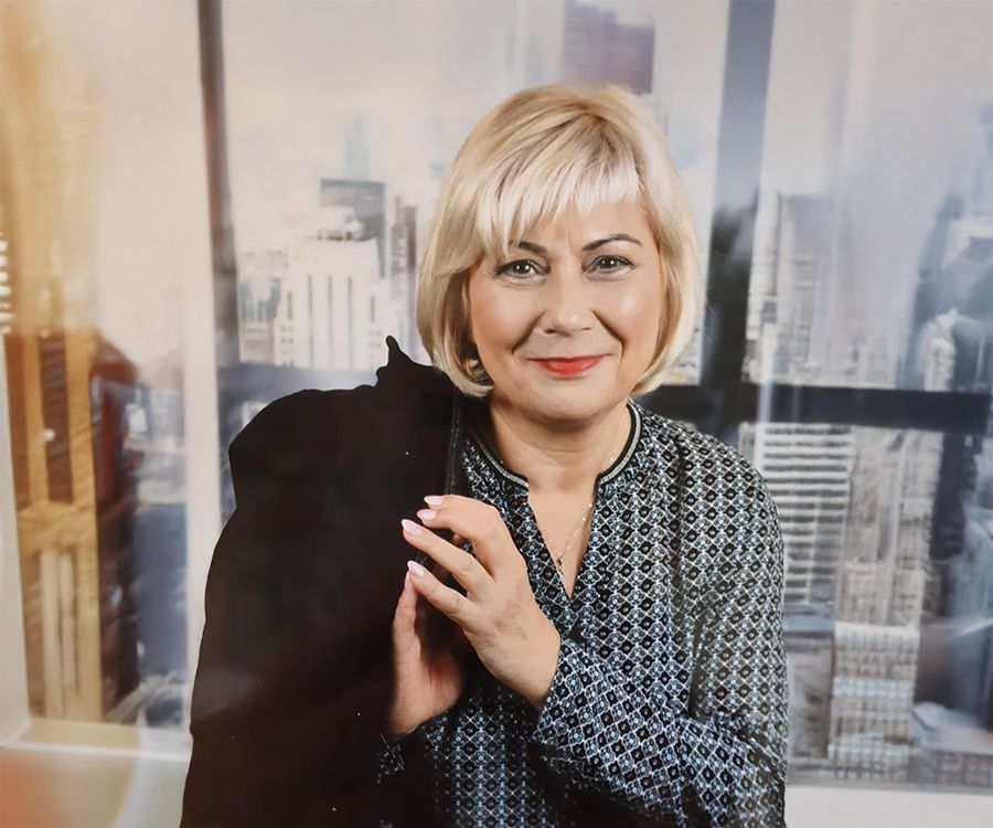 Eine Frau steht vor einem Fenster und hält eine Jacke über der Schulter.