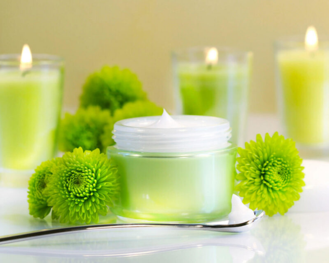 Ein Glas Sahne ist von grünen Blumen und Kerzen umgeben