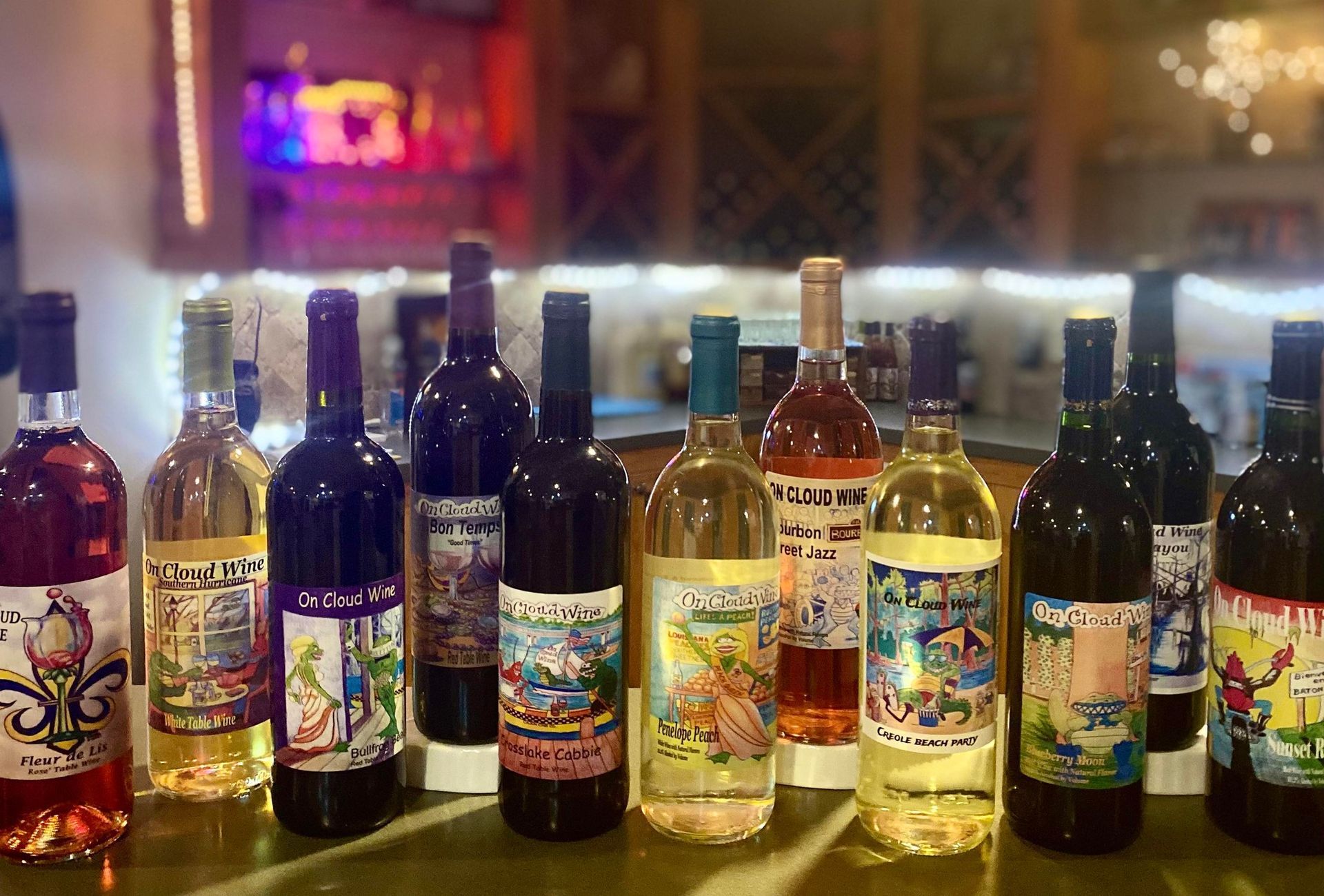 Bottles of wine on a bar, various colors, with illustrated labels; blurred background.