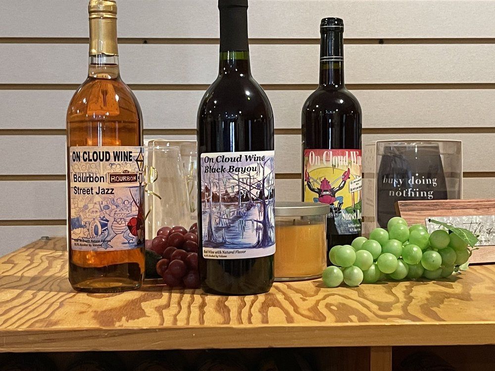 Three wine bottles and grapes on a wooden table. The wine is various colors, with labels, next to a glass and candles.