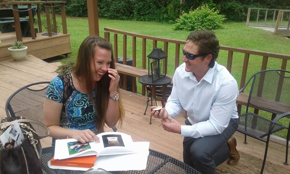 Man kneeling proposing to woman on a deck, both smiling, ring in hand.