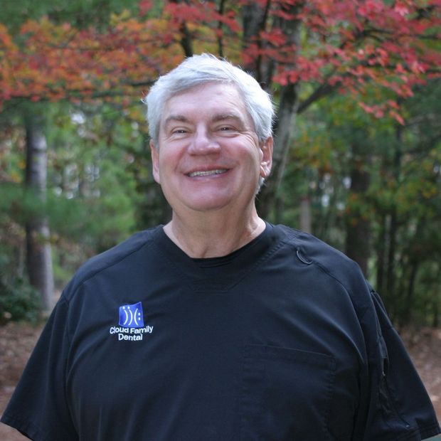 Smiling man in a black shirt standing outdoors with autumn trees in the background