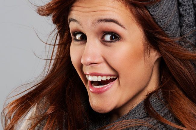 a woman wearing a hat and scarf is smiling with her mouth open .