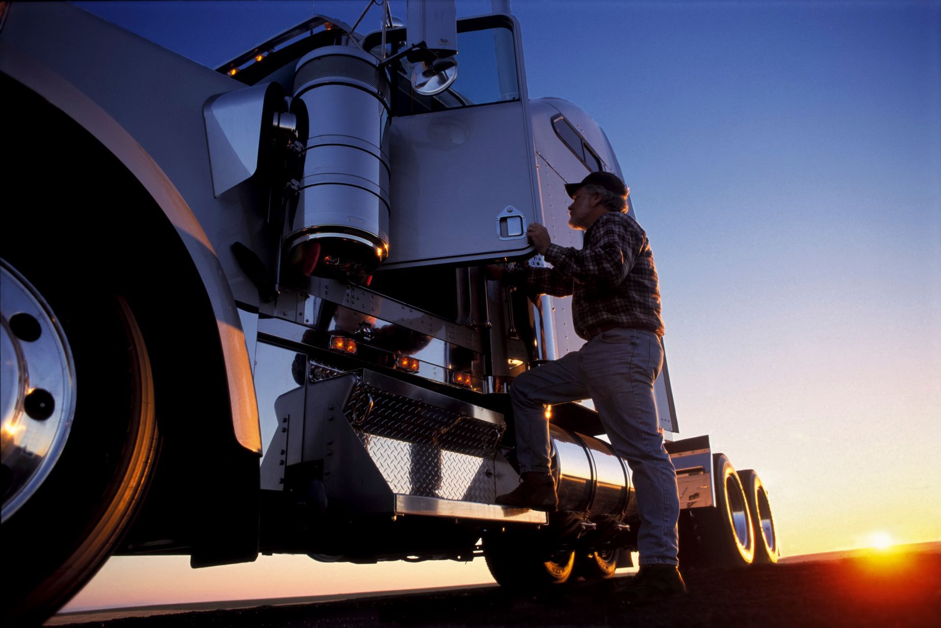 A man is working on a semi truck at sunset