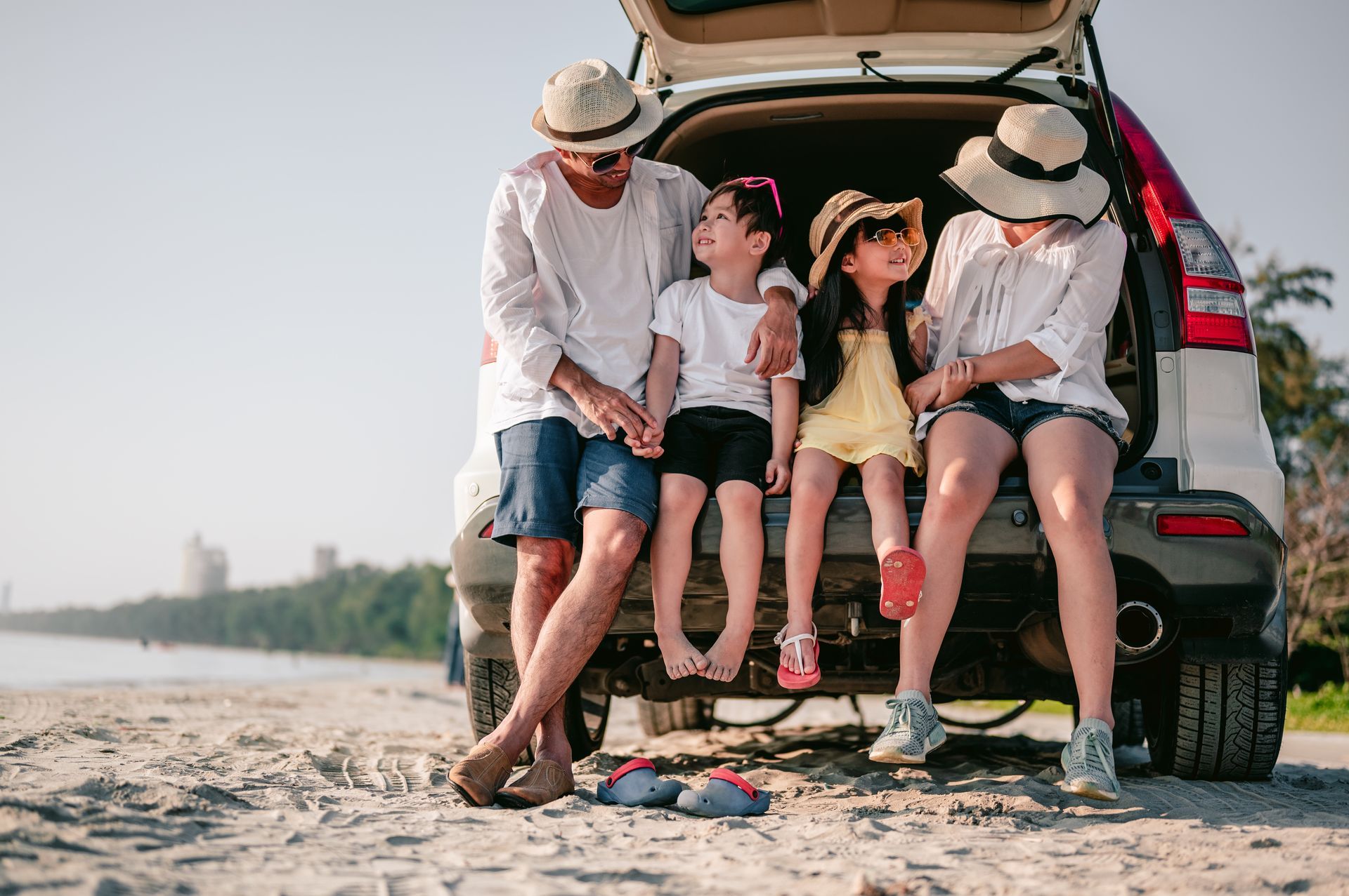 A family is sitting in the back of a car on the beach.