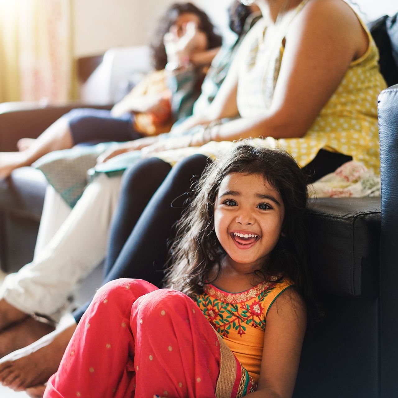 A little girl is sitting on a couch with her legs crossed and smiling.