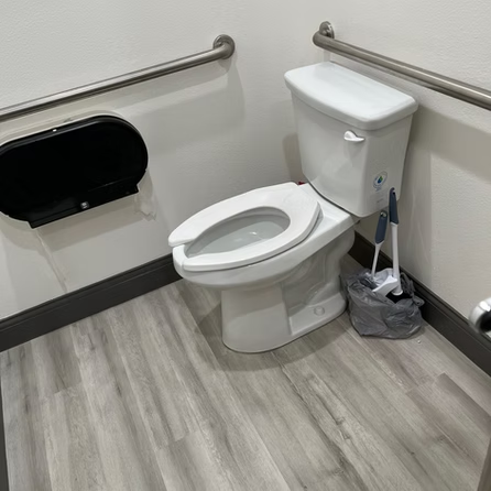 A white toilet is sitting on a wooden floor in a bathroom.