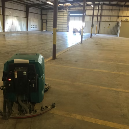 A green machine is sitting in the middle of an empty warehouse