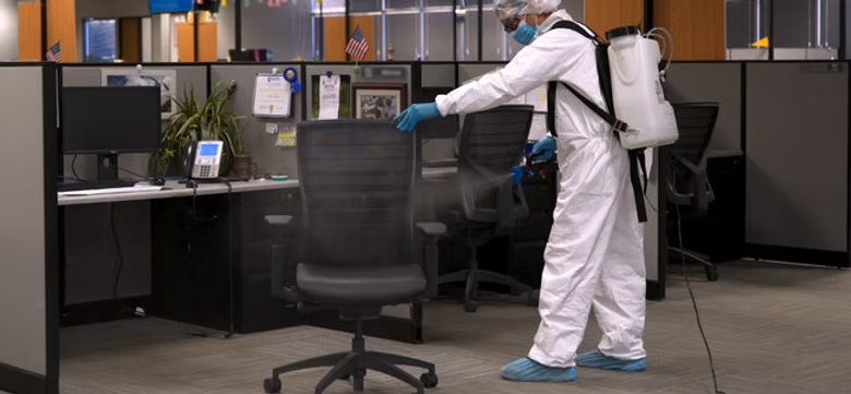 A man in a protective suit is disinfecting an office chair.