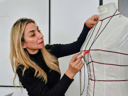 Mujer con suéter negro midiendo un maniquí de costura con una cinta métrica en un estudio.