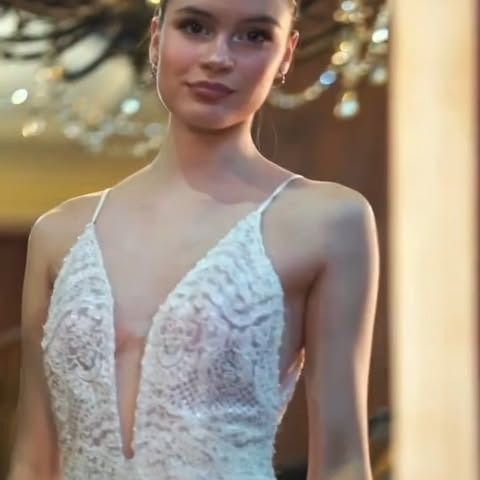 Mujer con un vestido blanco de encaje con escote pronunciado, de pie en el interior.