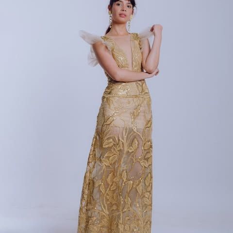 Mujer con un vestido de noche dorado de lentejuelas con bordados florales, posando con los brazos cruzados.