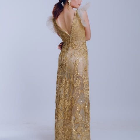 Mujer con vestido dorado bordado, espalda descubierta y mangas transparentes.