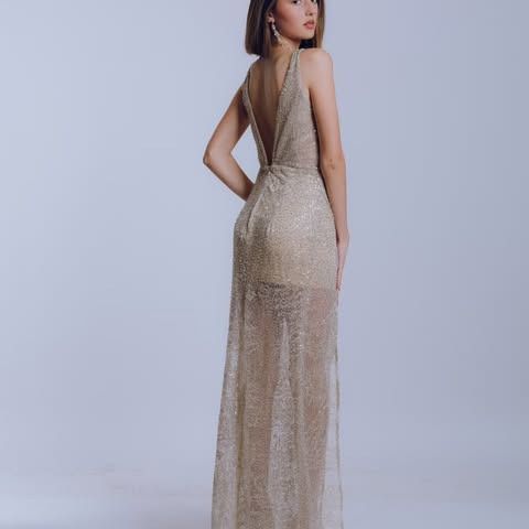 Mujer con un vestido de noche dorado y brillante, con un pronunciado escote, posando en un estudio.