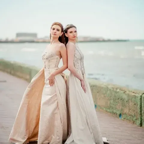 Dos mujeres con vestidos de gala están de espaldas en un paseo marítimo.