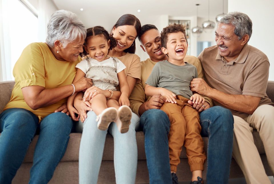 A large family is sitting on a couch laughing together.