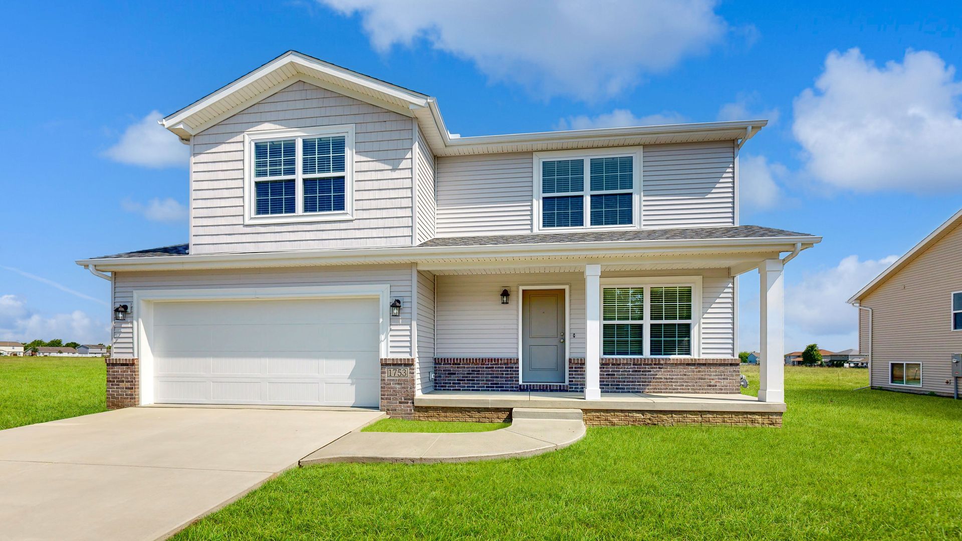 A large white house with a white garage door is sitting on top of a lush green field.