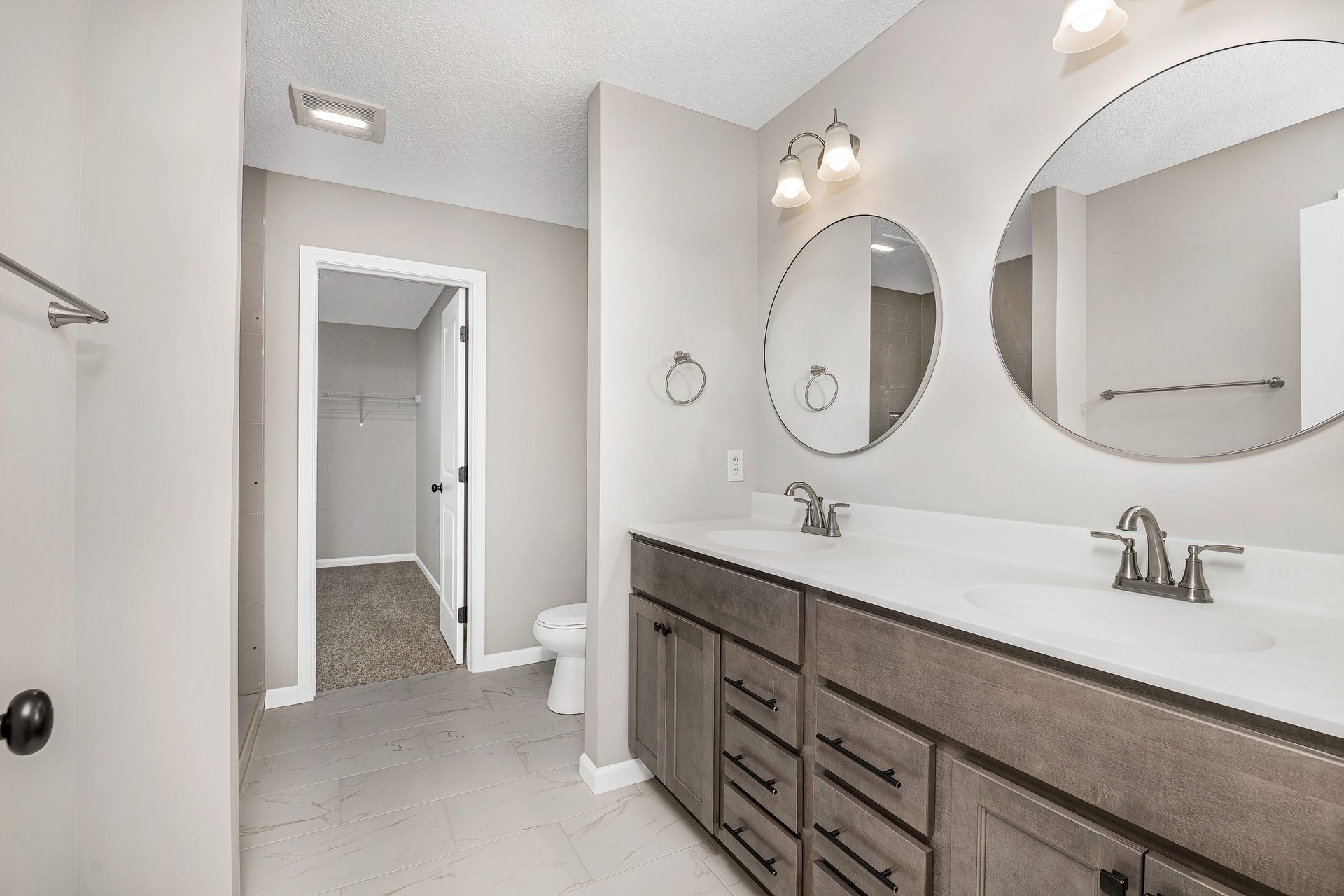 A bathroom with two sinks , two mirrors and a toilet.