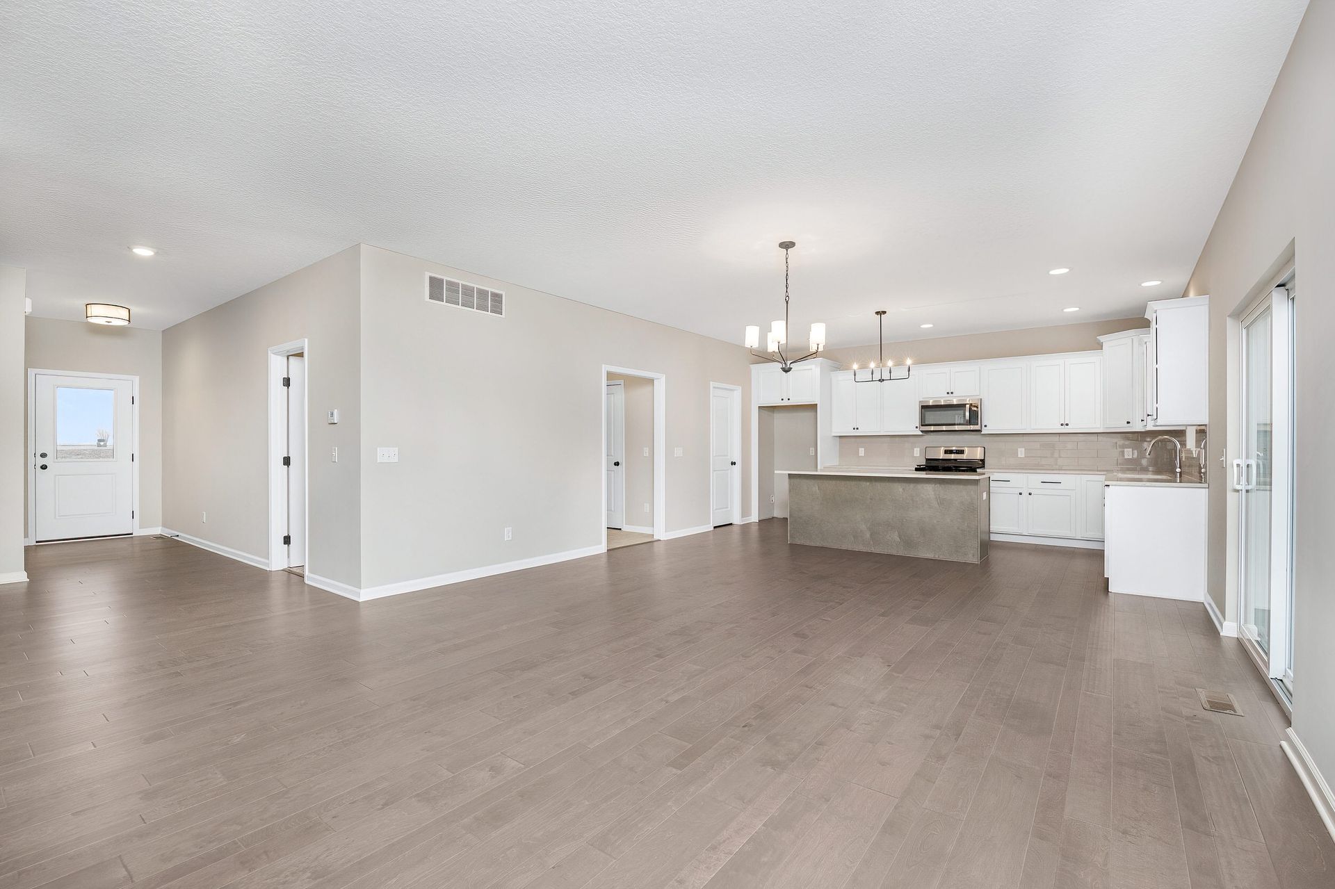 A large empty room with hardwood floors and a kitchen.