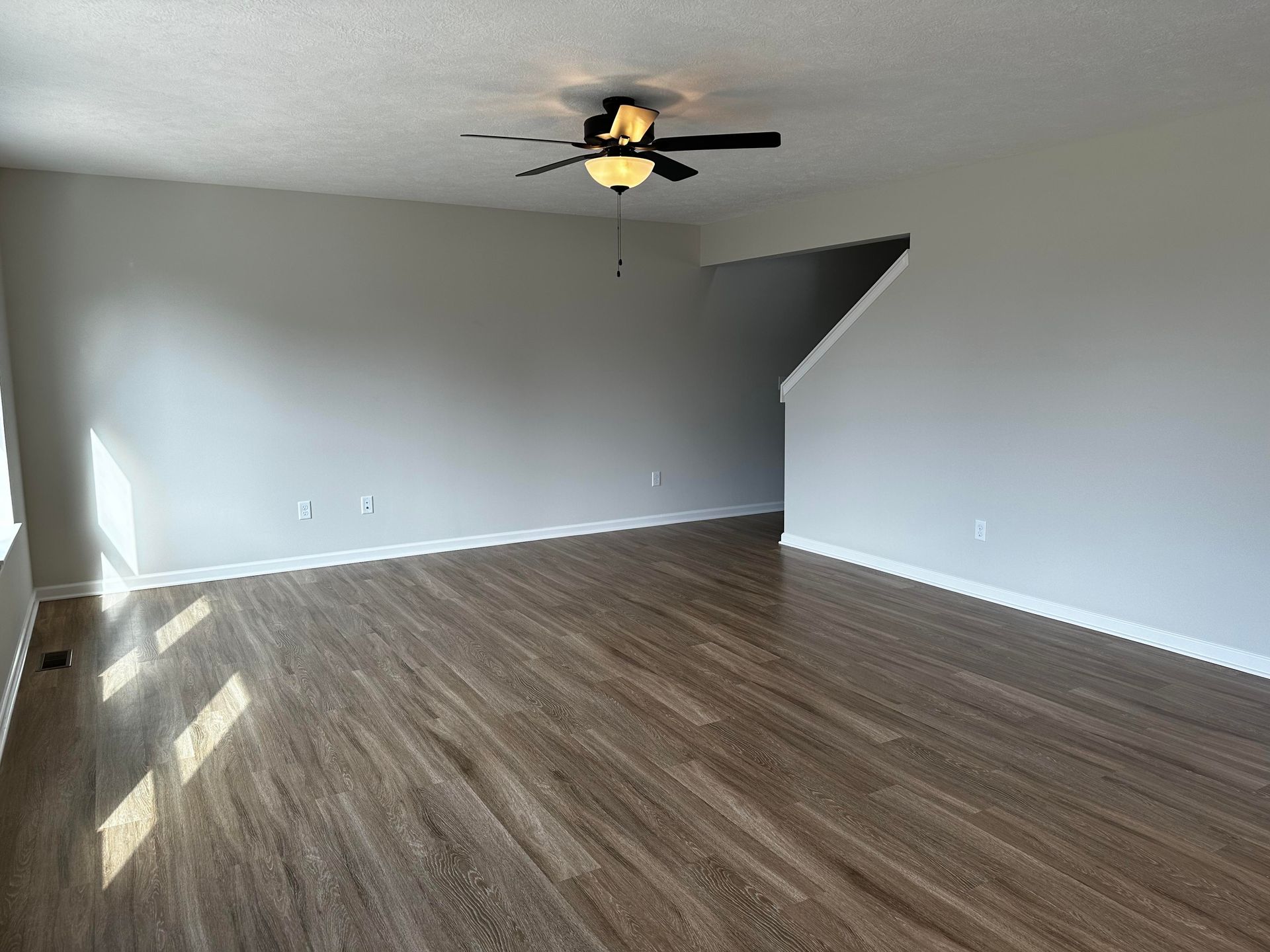 An empty living room with hardwood floors and a ceiling fan.