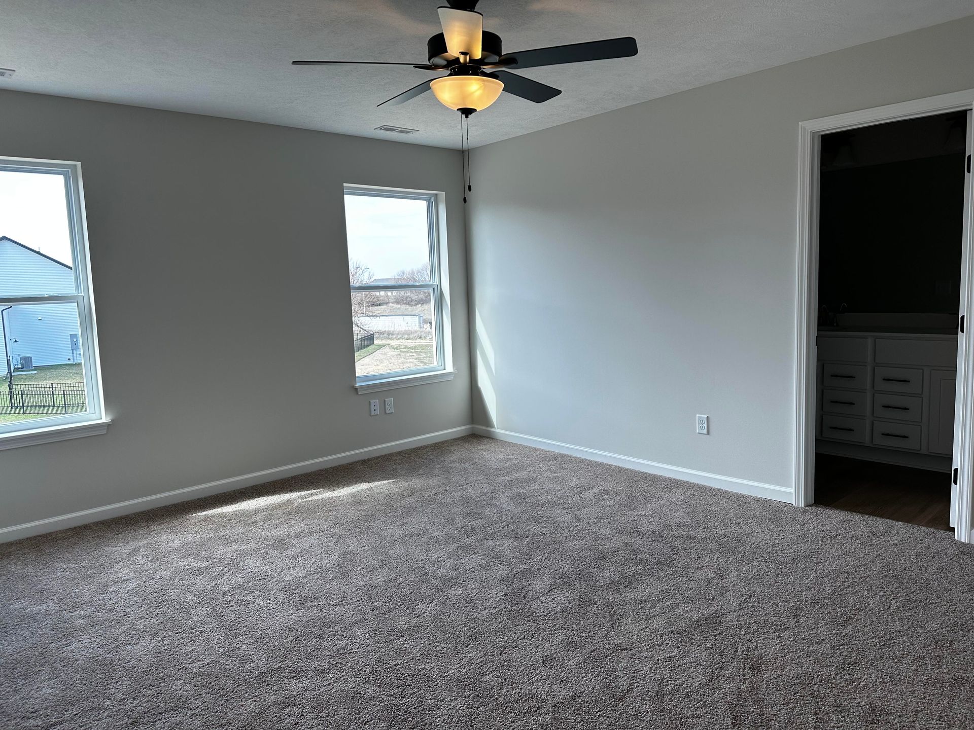 An empty bedroom with a ceiling fan and two windows