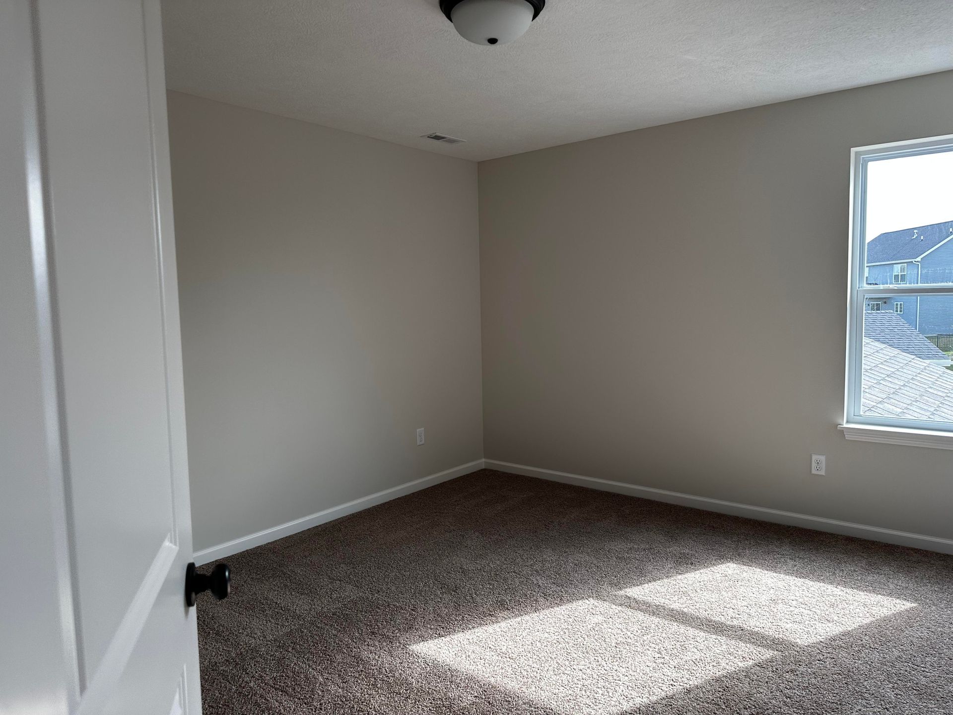 An empty bedroom with a window and a carpeted floor.