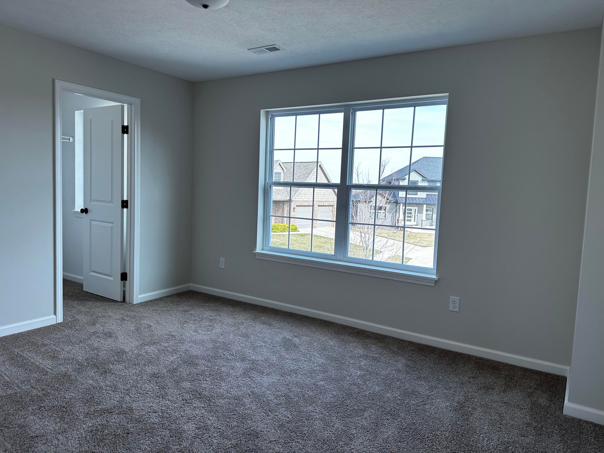 An empty bedroom with a large window and a carpeted floor.