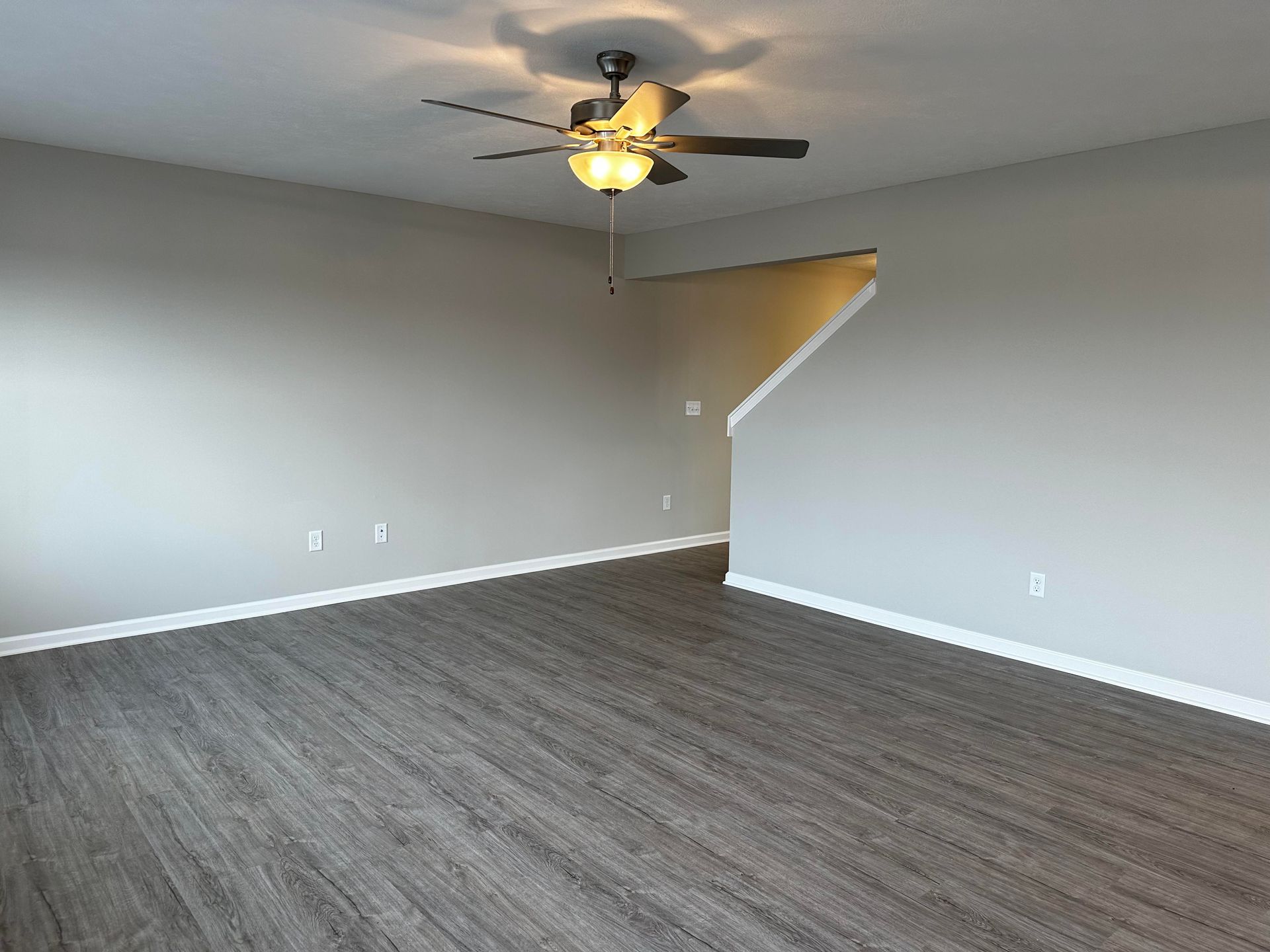 An empty living room with hardwood floors and a ceiling fan