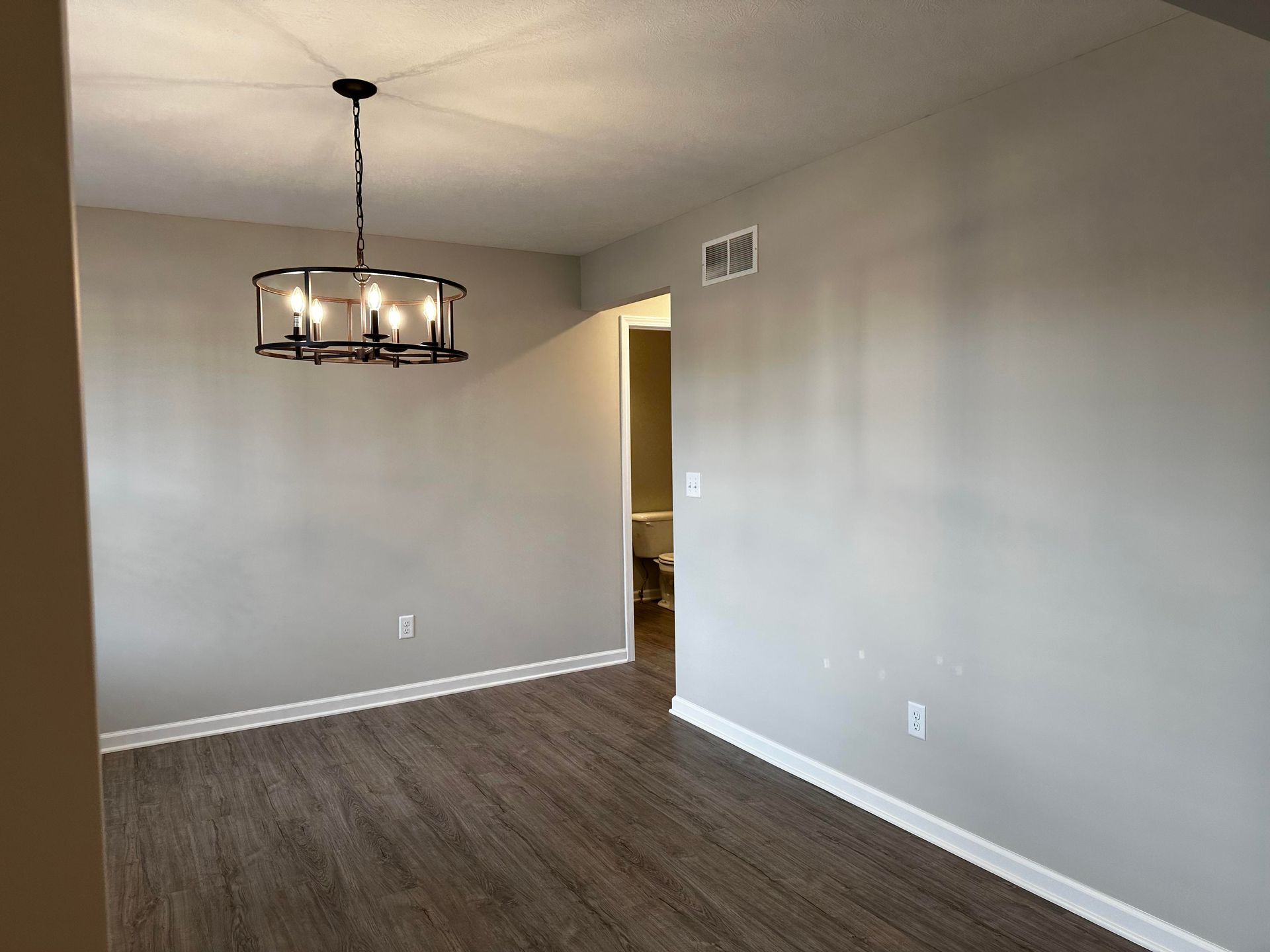 An empty dining room with a chandelier hanging from the ceiling.