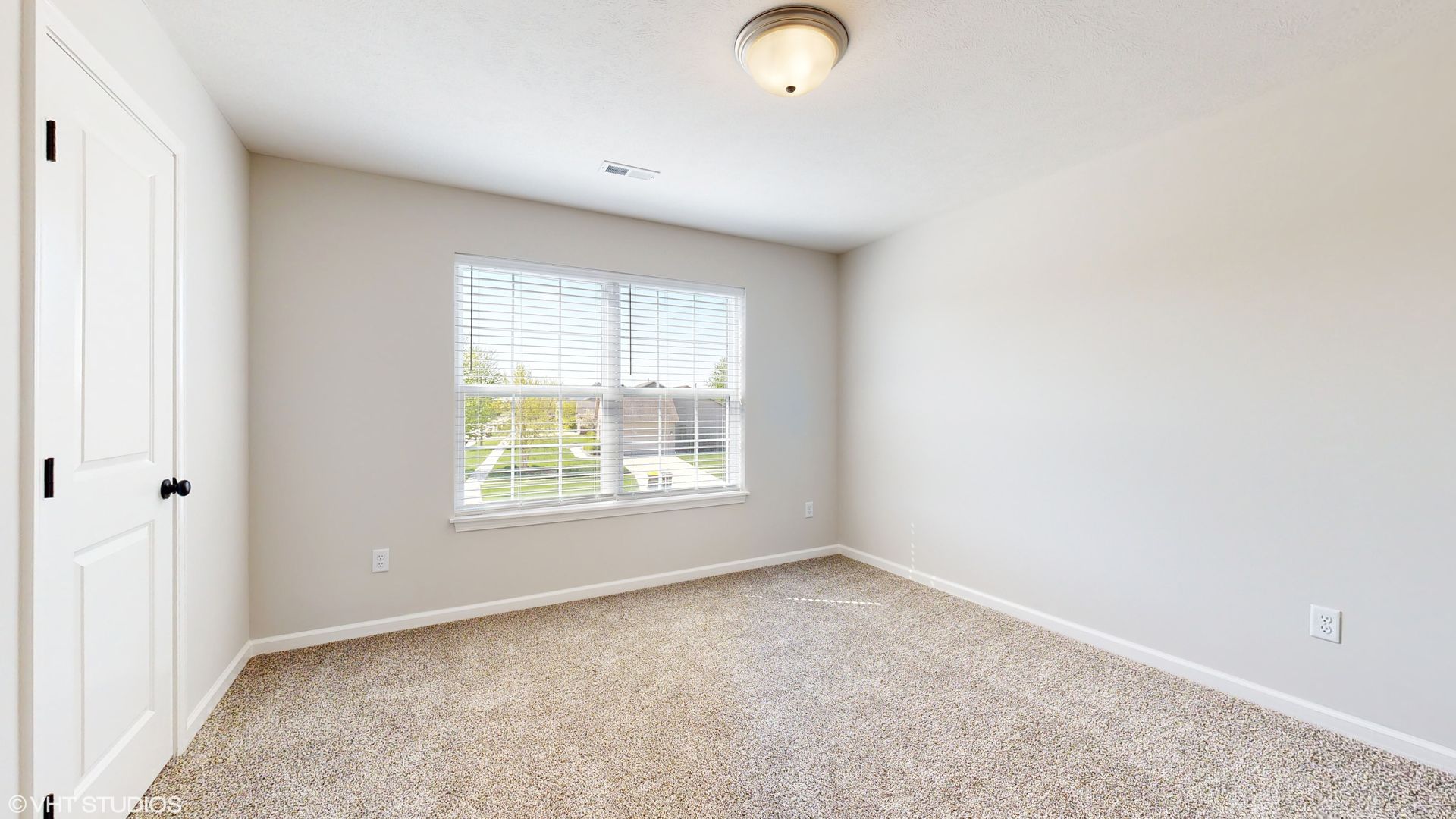 An empty bedroom with a window and a carpeted floor.