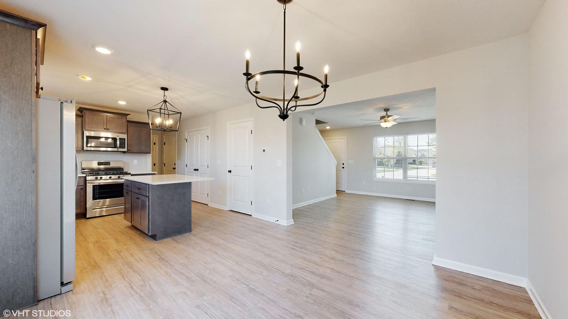 An empty living room with hardwood floors and a chandelier hanging from the ceiling.
