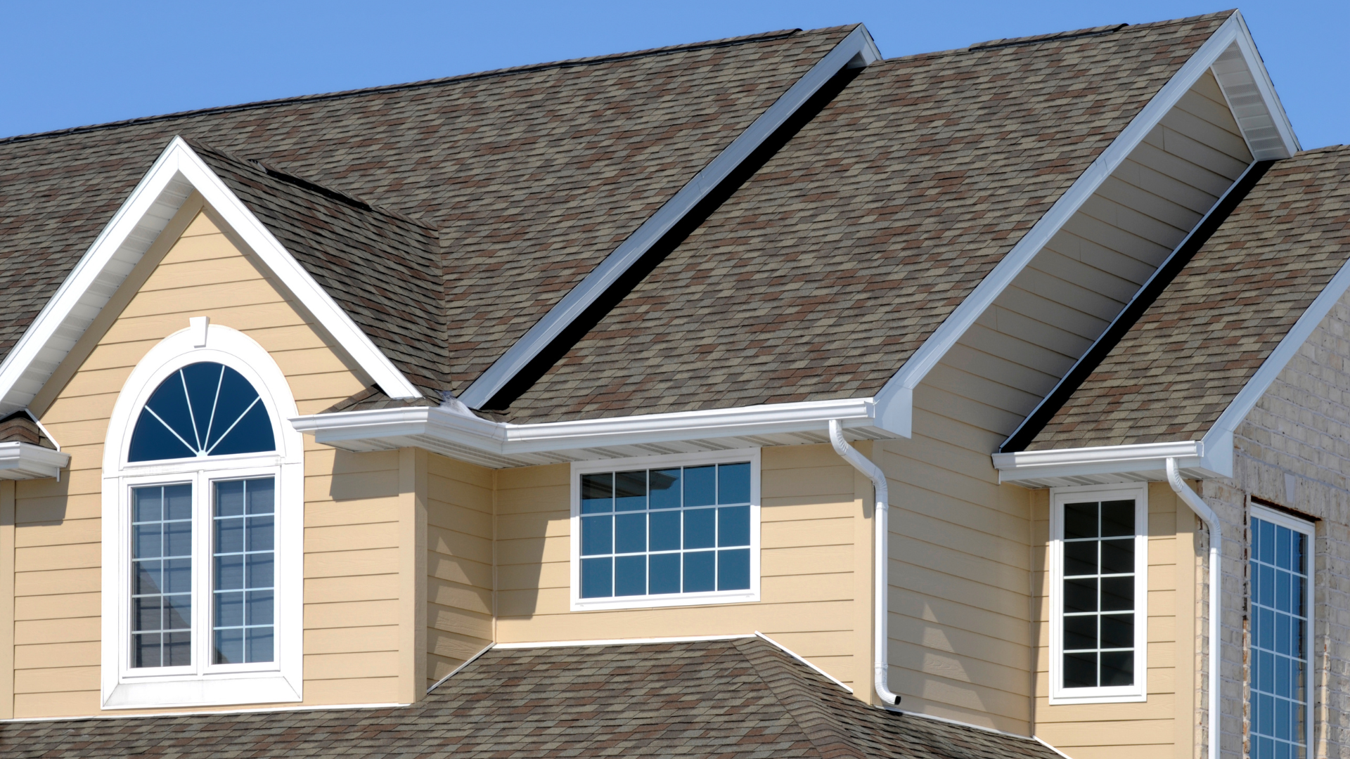 Beige suburban house roof with gray shingles, white trim, and arched windows