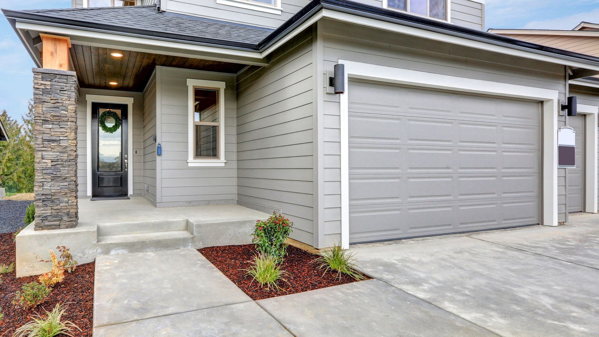 A large gray house with two garage doors and a wreath on the door.