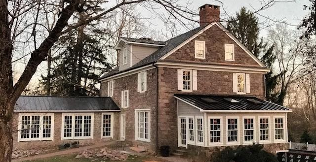 Two-story brick house with white trim, multiple windows, and a black roof, set amongst trees.