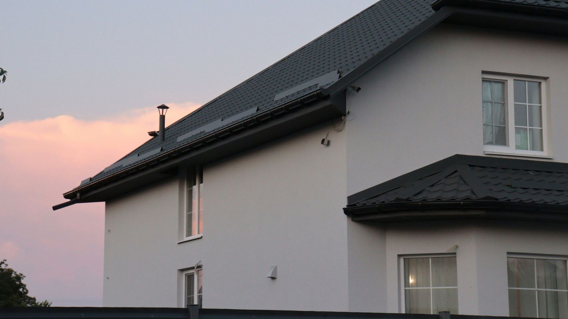 A white house with a black roof and a pink sky in the background