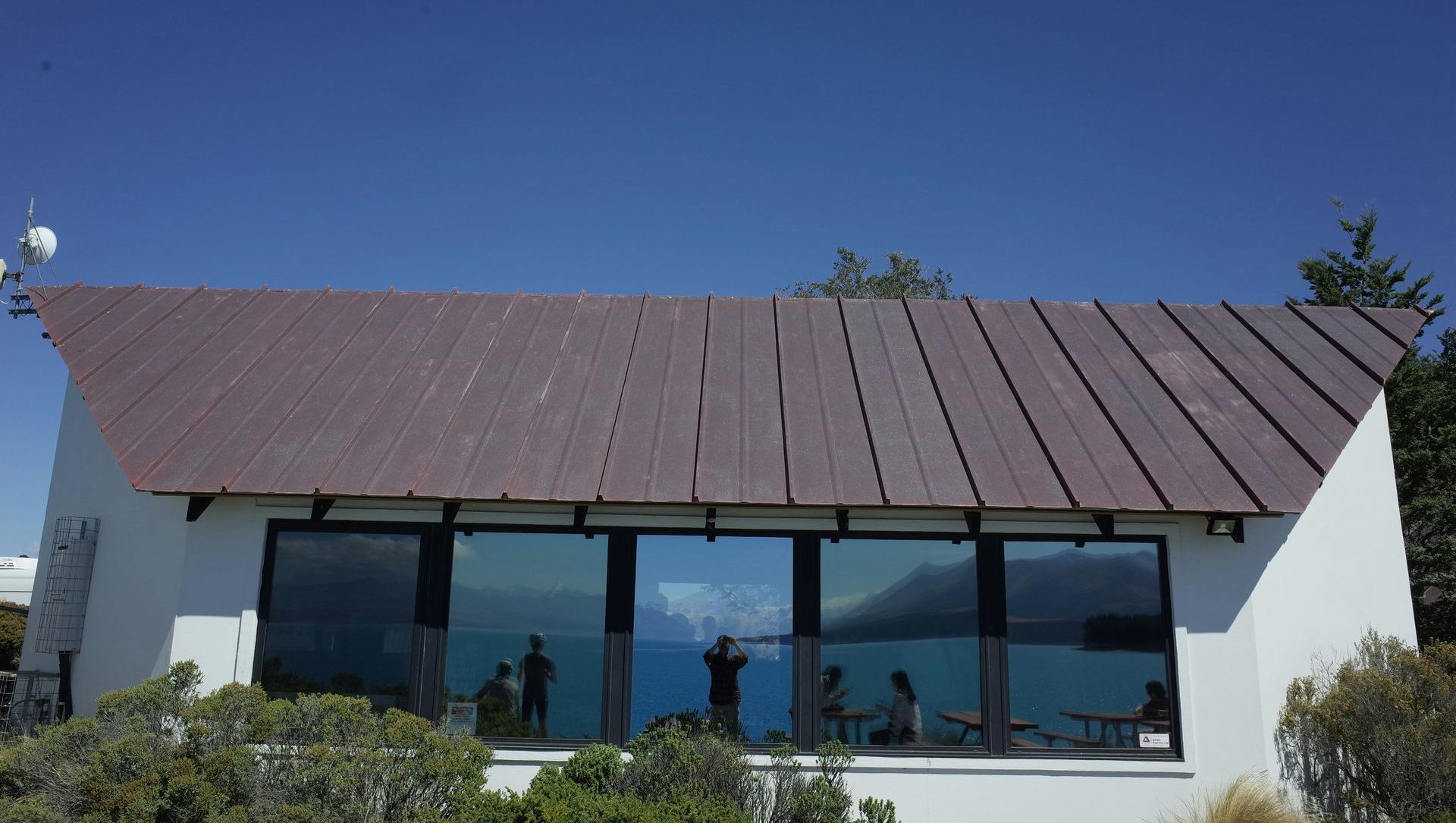 A white building with a brown roof and a lot of windows overlooking the ocean