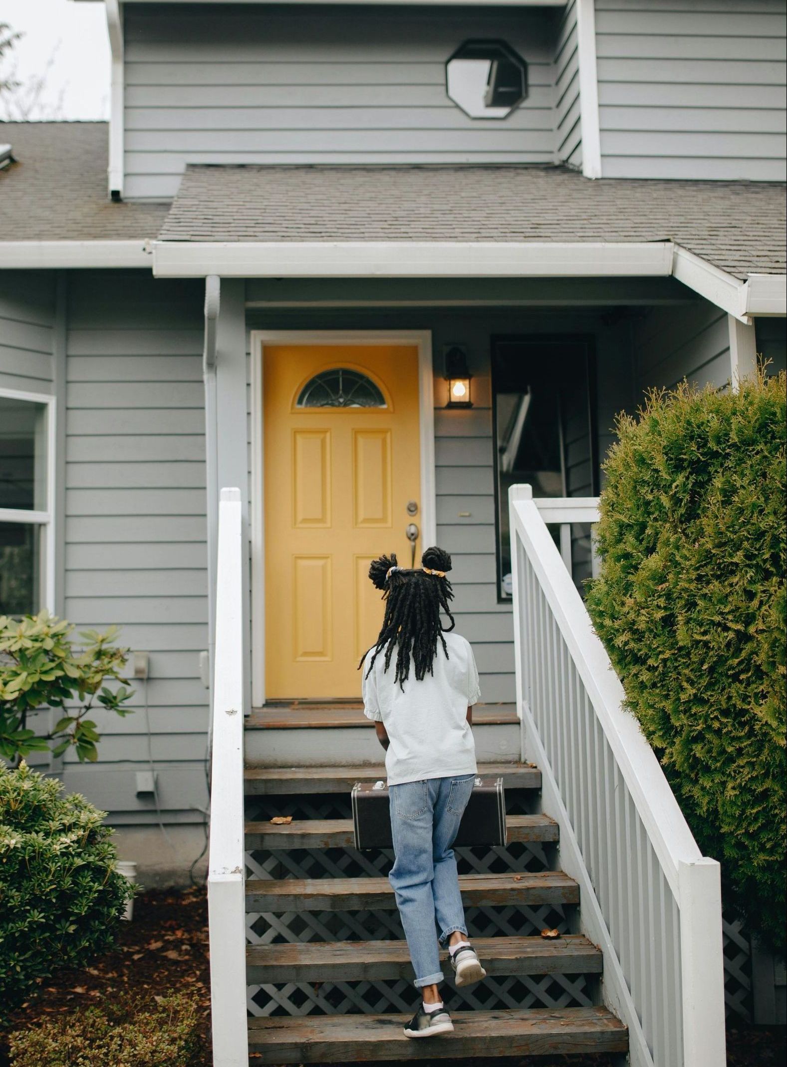 A woman is walking up the stairs to a house with a yellow door.