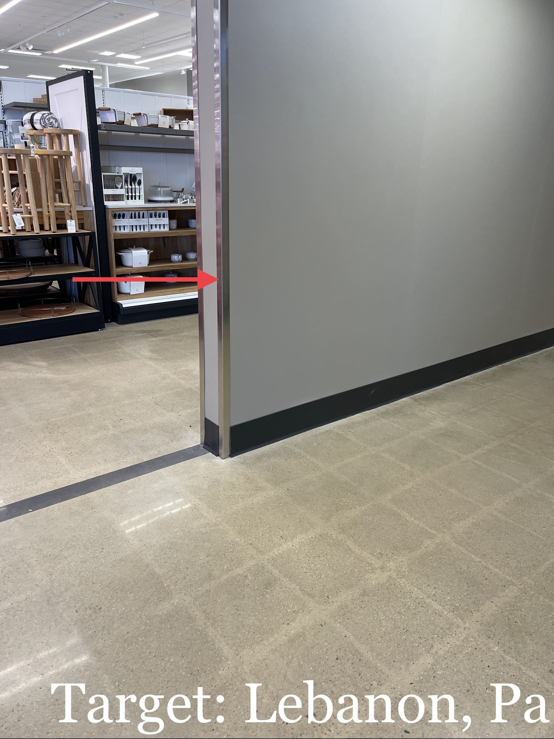Indoor store aisle beside a gray wall, with shelves and equipment in the background.