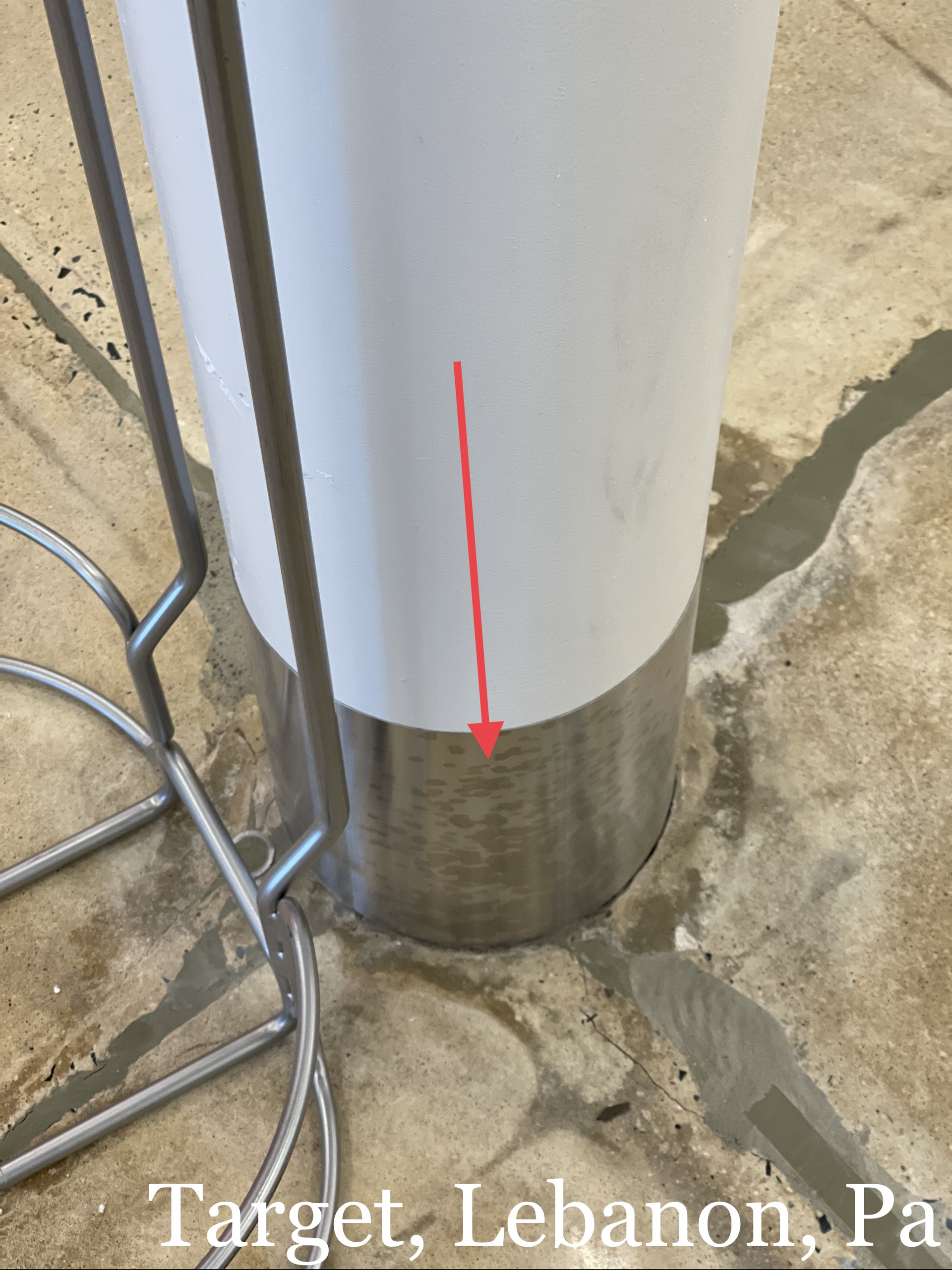 White pole with a rust-colored metal base on concrete, marked by a red arrow.